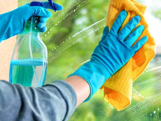 Limpieza de un vidrio con guantes azules, atomizador y paño de microfibra.