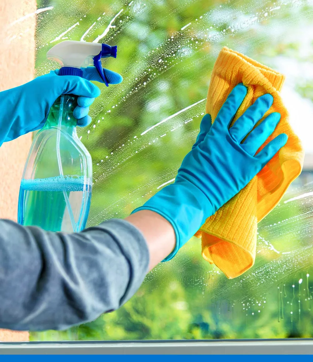 Limpieza de un vidrio con guantes azules, atomizador y paño de microfibra.